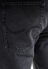 Primer plano de un bolsillo trasero de jeans de mezclilla negra con un detalle de costura curva en el lado derecho de la cadera del portador.