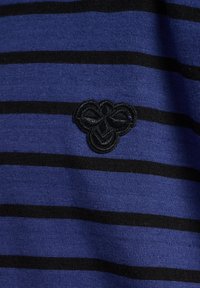 Blauw-zwart gestreepte stof met een zachte textuur; heeft een geborduurd zwart bijenlogo aan de linkerkant.