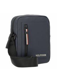 Borsa a tracolla blu navy con tessuto testurizzato, chiusura con zip, tracolla regolabile e dettaglio del logo in bianco. Presenta un accento a righe.