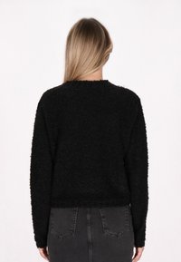 Schwarzer, kuscheliger Pullover mit lockerer Passform, Rundhalsausschnitt und langen Ärmeln. Mit strukturiertem Material und verkürzter Länge. Kombiniert mit hoch taillierten Jeans.