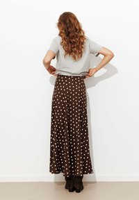 Jupe maxi à pois bruns avec un design fluide et une texture douce, assortie à un t-shirt gris et des bottes de cheville noires.