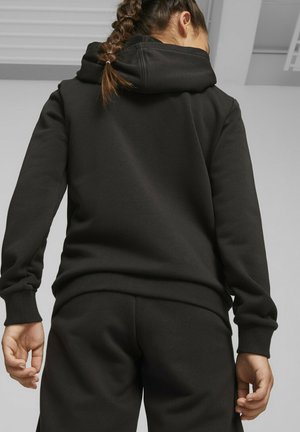 Sudadera negra con un ajuste ceñido, que presenta una gran capucha y puños acanalados. La tela tiene una textura suave, combinada con pantalones de chándal a juego.