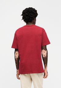 Κόκκινο κοντομάνικο μπλουζάκι από βαμβάκι, με στρογγυλή λαιμόκοψη και απλό σχέδιο με άνετη εφαρμογή. Ορατές ραφές στα μανίκια.