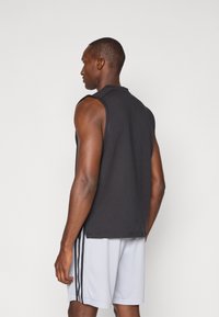 T-shirt sans manches noir avec un col rond et un short de sport gris contrastant avec des rayures sur les côtés. Texture de tissu lisse.