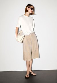 Lichtbeige suède culottes met een rechte snit en een split aan de voorkant, gecombineerd met een eenvoudig wit T-shirt en zwarte teenslippers.