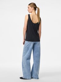 Juoda be rankovių palaidinė su žemu nugara, derinama su šviesiai mėlynomis plačiomis kelnėmis ir juodais batais. Lygus audinys ir kasdieniškas dizainas.