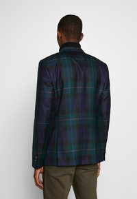 Geruite blazer in donkergroen, marineblauw en zwart. heeft een gestructureerde silhoeët, met een notch-kraag en knoopmanchetten. Glad materiaal met zichtbare textuur.