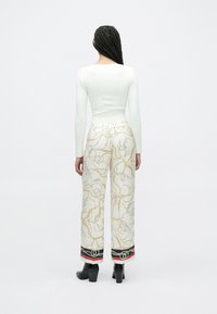 Valge soonikkoes pikkade varrukatega särk, mida on kombineeritud laia säärtega pükstega, millel on kuldse kettmustri, musta ja punaste aktsentidega ning pahkluukõrgustega mustade kontsadega.