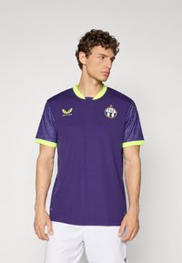 Maillot de sport violet à manches courtes, avec un col vert vif et des accents sur les manches, logo sur la poitrine et un motif texturé sur les manches.