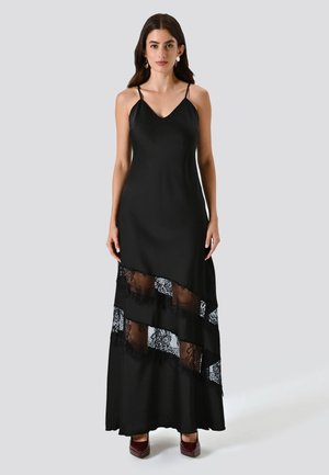 Schwarzes Maxikleid mit Spaghettiträgern, das am Saum mehrschichtige, durchsichtige Spitzenpaneele und eine glatte, satinartige Oberfläche aufweist.