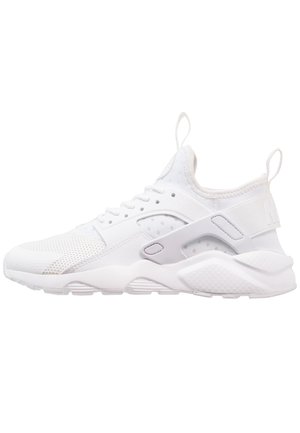 Baskets de sport blanches avec tige en mesh, semelle épaisse et amortissante, languettes de traction au talon et à la languette, et bandes latérales en plastique de soutien.