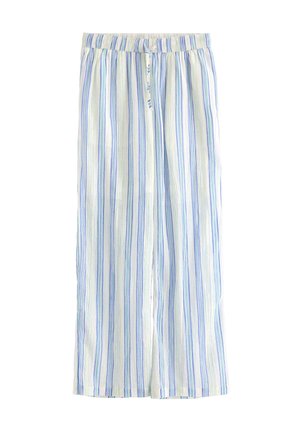 Smilende pige står iført hvid T-shirt med blåt søhestprint, løse hvide bukser med blå striber, hvide sandaler og armbånd.