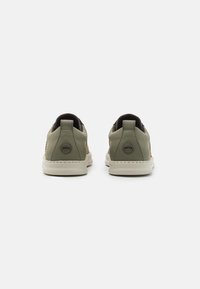 Gröna canvas-sneakers med en texturerad yta, med en vit gummisula och svarta detaljer vid hälen. Logotyp synlig på baksidan.