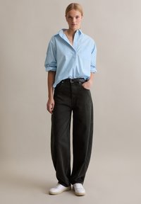 Camicia azzurro chiaro con bottoni e taschino sul petto, abbinata a pantaloni larghi verde scuro e sneakers bianche. Design semplice e vestibilità comoda.