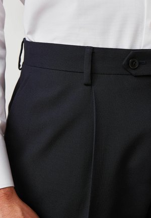 Pantalones ajustados de color navy oscuro con una textura suave, que presentan un cierre de botón, pasadores para cinturón y pliegues frontales para una apariencia elegante.