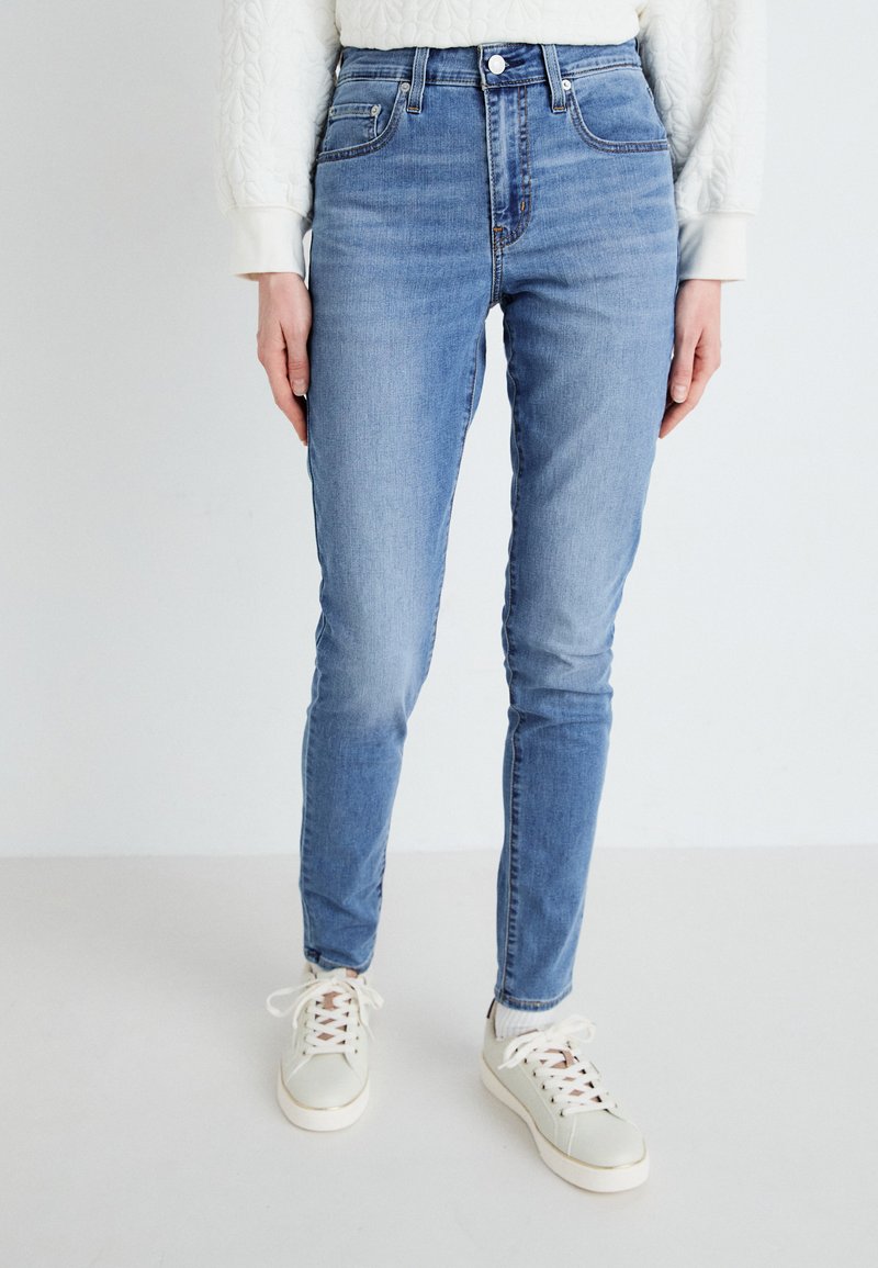 Höga, slim-fit jeans i ljusblå denim. Har framfickor, sömmar och en knäppning. Kombineras med vita sneakers.