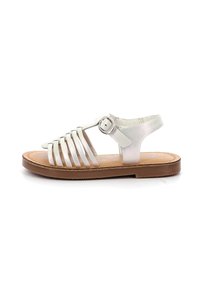 Sandalias de cuero blancas con tiras, que cuentan con múltiples tiras a través del pie, una correa para el tobillo con hebilla, y una suela marrón con un patrón texturizado.