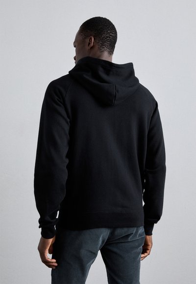 Sort hoodie med hætte, lange ærmer og en afslappet pasform. Lavet af blødt materiale med ribbede manchetter og kant. Modellen vender væk fra kameraet.
