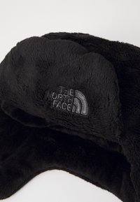 Sort vinterhat med pelsfor og blød tekstur, med et broderet logo af "The North Face" på forsiden.