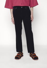 Černé manšestrové kalhoty s rovnými nohavicemi, spárované s černými sandály s jasně oranžovými a žlutými pásky.