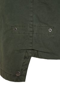 Ciemnozielony, teksturowany materiał z detalami szwów; posiada napy na dole oraz boczne rozcięcie, co zwiększa swobodę ruchu i wentylację.