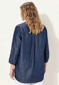 Camicia di jeans con maniche a tre quarti, vestibilità ampia e yoke posteriore arricciato, caratterizzata da un intenso colore blu e tessuto texturizzato.