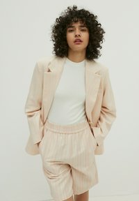 Helles rosa Anzugset mit einem Blazer mit vertikalen Streifen, kombiniert mit passenden knielangen Shorts. Der Blazer hat eine lockere Passform und keine Knöpfe.