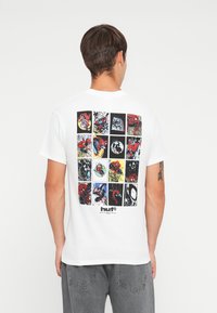 Camiseta de algodón blanca con un estampado gráfico de paneles de cómic en la parte posterior, predominantemente en colores rojo, negro y amarillo.