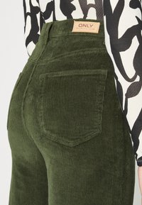 Groene corduroy broek met een hoge taille, verticale ribbeltextuur en twee achterzakken. De tailleband heeft een tan label met "ONLY" merk uiting.