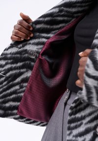 Wollen blend jas met zwart en grijs gestreept patroon, met een bordeauxkleurige gevoerde voering en een grote knoopsluiting.