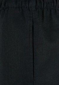 Tissu noir avec une poche verticale à fente et une ceinture élastique froncée, montrant la texture et les coutures détaillées.