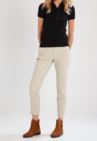 Svart pikétröja med kort ärm och knappar, beige slim-fit byxor och bruna mocka ankle boots med elastiska sidopaneler.