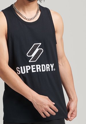 Sort bomuldstanktop med rund halsudskæring, der har et hvidt "SUPERDRY" logo og emblem på forsiden. Sølv kædedesign synligt.