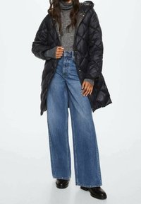 Sort quiltet dunjakke med hætte, båret over en grå rullekravetrøje, parret med højtaljede, vidde ben blå denimjeans og sorte støvler.