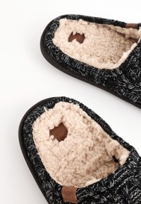 Chaussons noirs et gris avec une doublure en fourrure beige douce, présentant une tige texturée et un petit écusson logo en cuir marron.