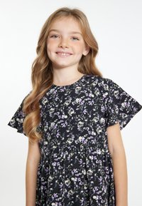 Bloemenjurk van zwarte stof met korte fladdermouwen, voorzien van paarse en witte bloemenpatronen, en een geraffineerde taille.