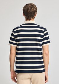 Mörkblå och krämfärgad randig polo skjorta med korta ärmar, krage och rak fåll. Slät tyg med en avslappnad passform.