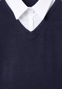 Maglione blu navy con scollatura a V indossato sopra una camicia bianca con colletto. Il tessuto è liscio, con cuciture visibili lungo i bordi.