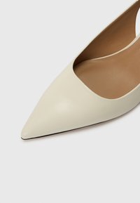 Talons à bout pointu en cuir beige doux, avec une découpe profonde sur les côtés, texture lisse et semelle noire pour le contraste.