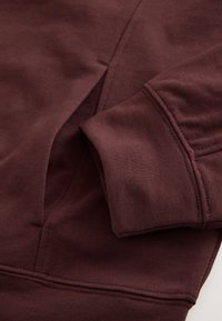Close-up of a brown sweatshirt sleeve and front pocket with visible stitching details on soft fabric.