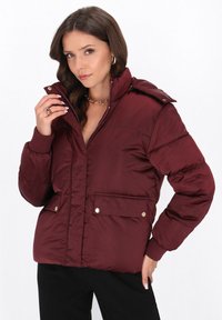 Giacca imbottita bordeaux con bottoni a pressione, colletto alto, due tasche anteriori, polsini a coste e texture trapuntata.