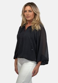 Czarna bluzka w kropki o luźnym kroju, lekka tkanina i dekolt w serek. Posiada obszerne rękawy i sznurek na dole.