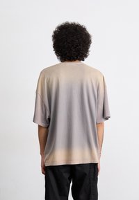 Oversized short-sleeve shirt in gradient gray and beige tones, featuring a soft texture and a casual cut without visible logos or embellishments.
