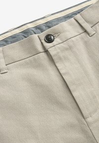 Pantalons texturés beiges avec fermeture à bouton, détails de couture subtils et une ceinture intérieure contrastante en bleu marine.