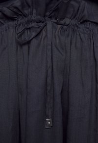 Lähikuva tummasta kankaasta, jossa on r gathered elastic vyötärö ja sidottu nauha, jossa on pieniä metallisia neliöpäitä.