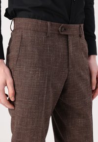 Pantaloni maro cu un model, realizati dintr-un material texturat cu un luciu subtil, având un front plat, buzunare laterale și o închidere cu nasture la talie.