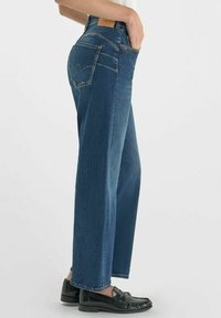Donkerblauwe high-waisted jeans met een rechte pijp, met contrasterende stiksels en een leren label op de achterkant van de tailleband.