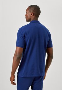 Mørkeblå kortærmet polo-shirt med struktureret stof, ribbede kraver og sideslidser i bundet for nem bevægelse.