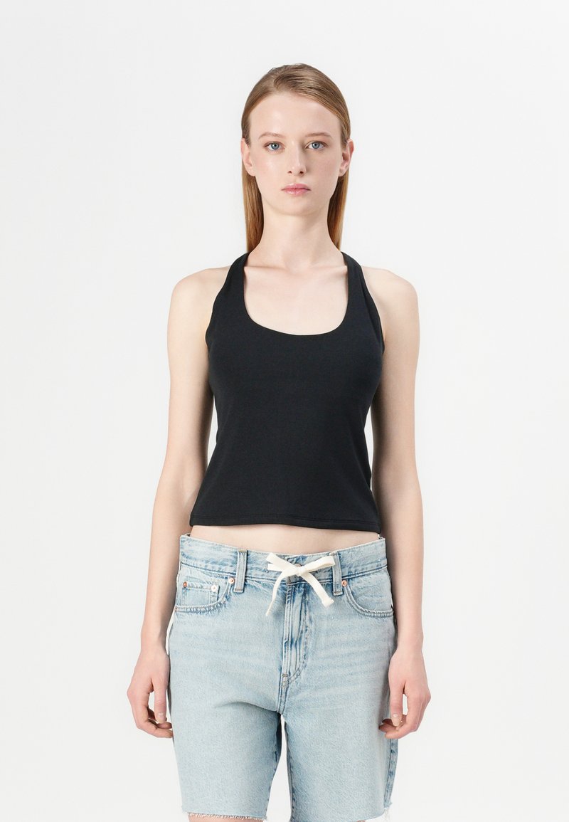 Black cropped tank top with a scoop neckline, made of soft fabric. Worn with light blue high-waisted denim shorts featuring a drawstring.