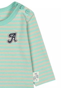 Mintgrünes und beiges gestreiftes Langarmshirt mit rundem Ausschnitt, Knopfakzenten an der Schulter und einem gestickten Buchstaben "A" auf der Brust.